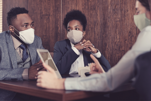 Workers sitting at a table talking and wearing masks