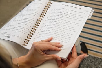 A woman turning the page of a spiralbound transcript