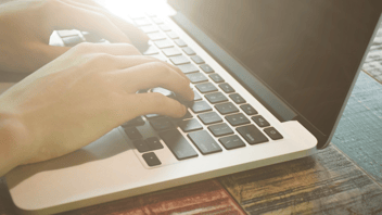 A man's hands typing on a Mac laptop.