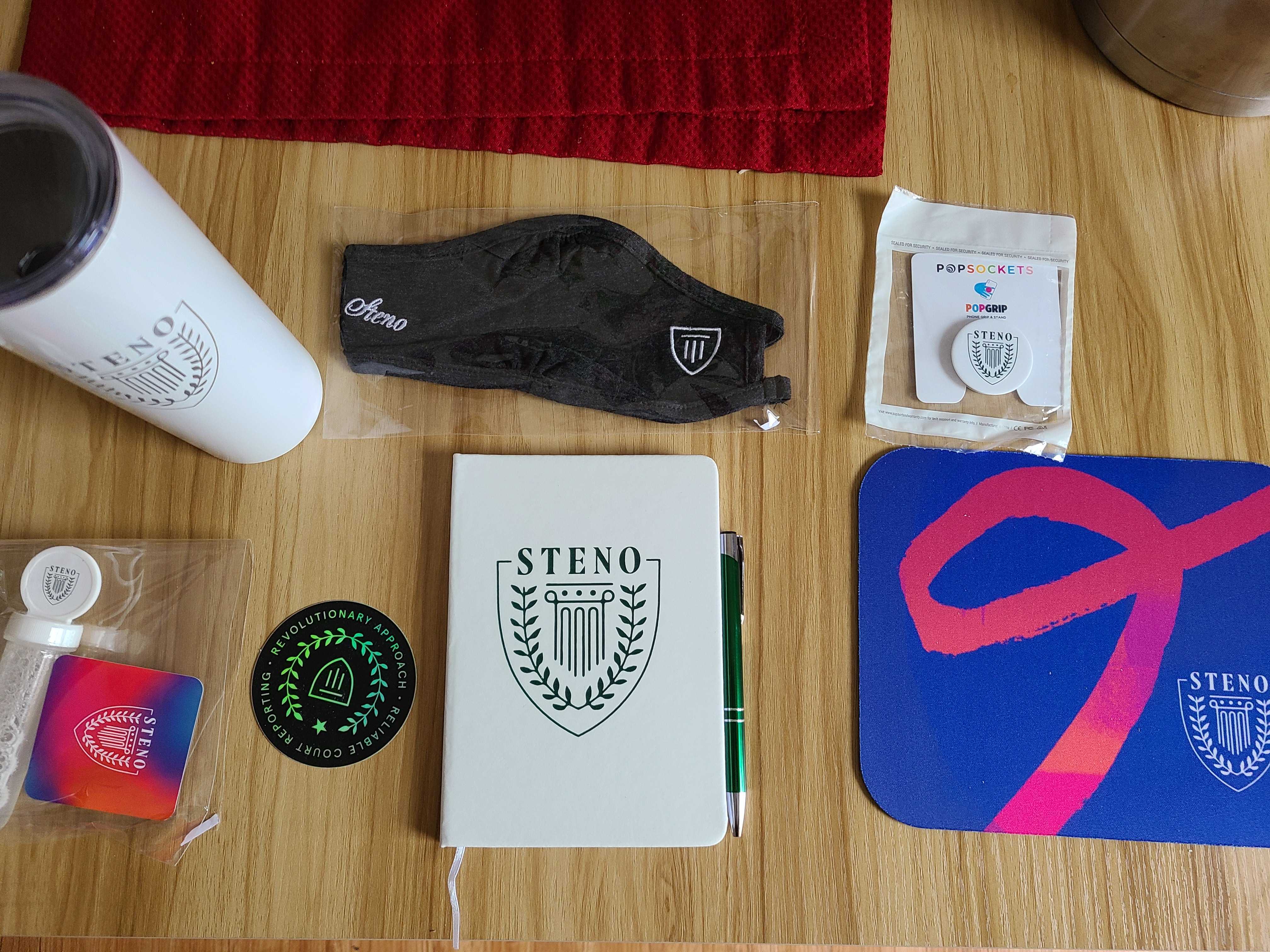 Looking down at a desk containing Steno swag items: travel cup, notebook, mask and more.