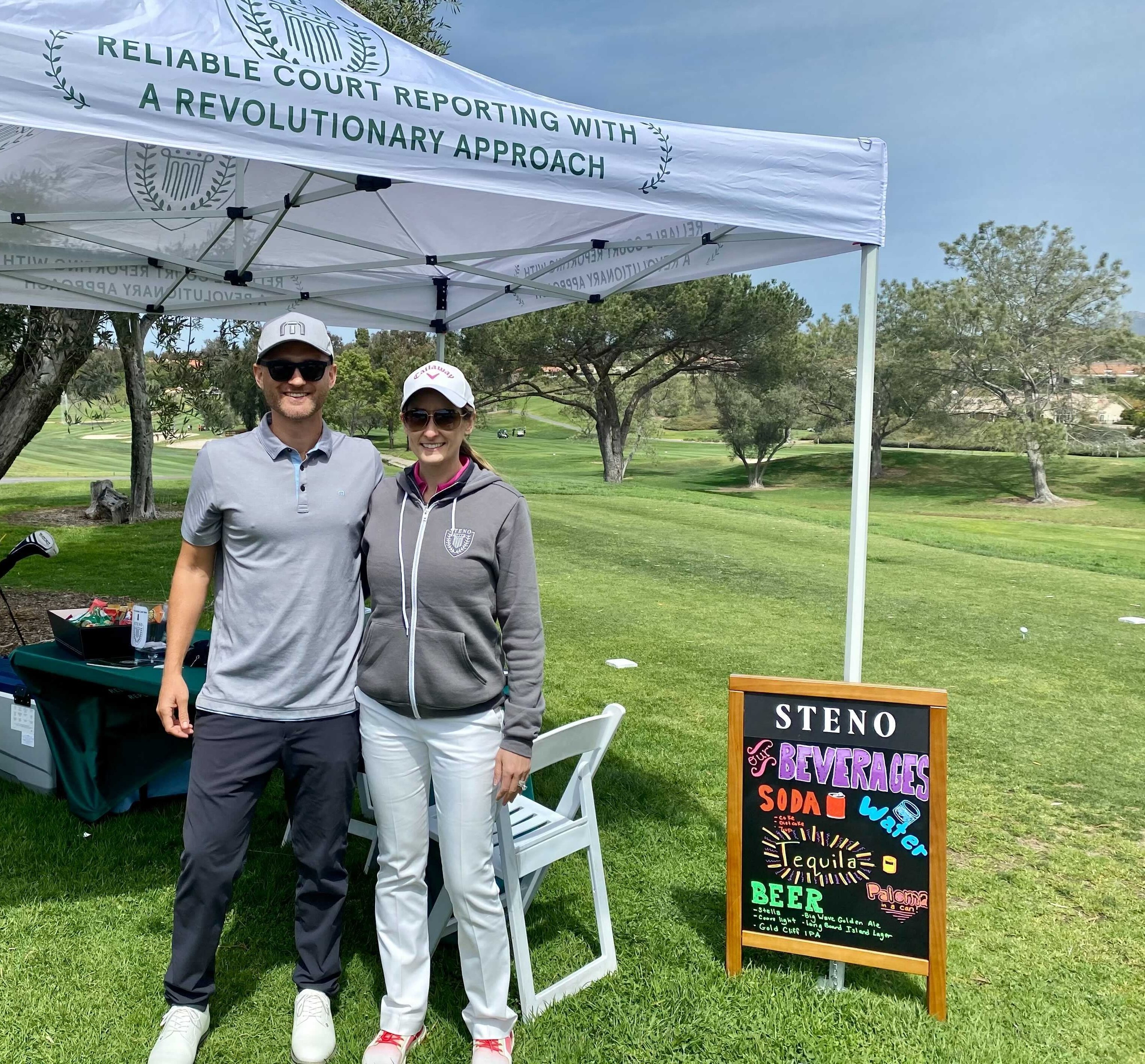 Connor and Carmela stand in front of a Steno-branded tend on a golf course.