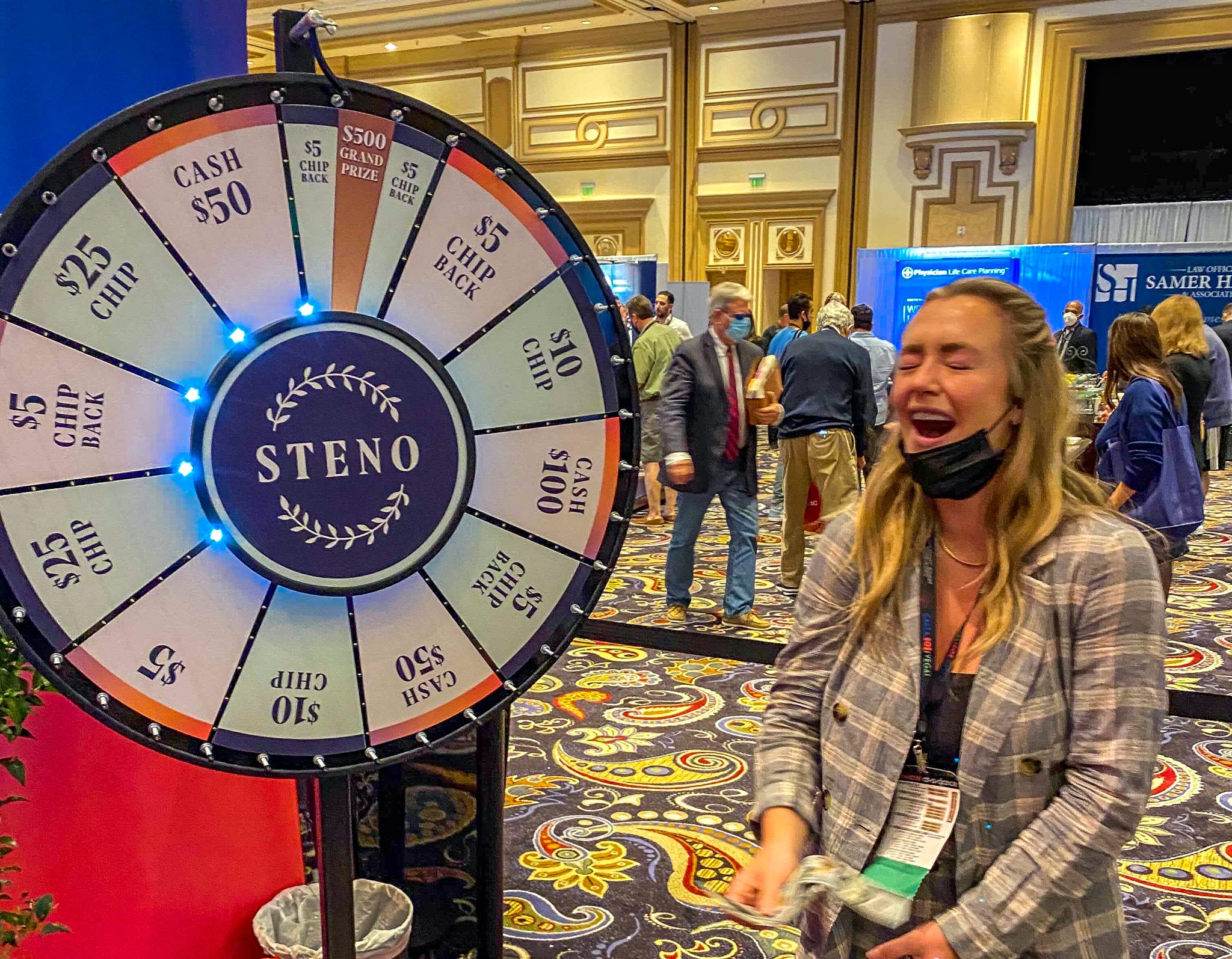 A blonde woman smiles with her eyes closed and in the background a light-up prize wheel has landed on a space that says "$500 grand prize"