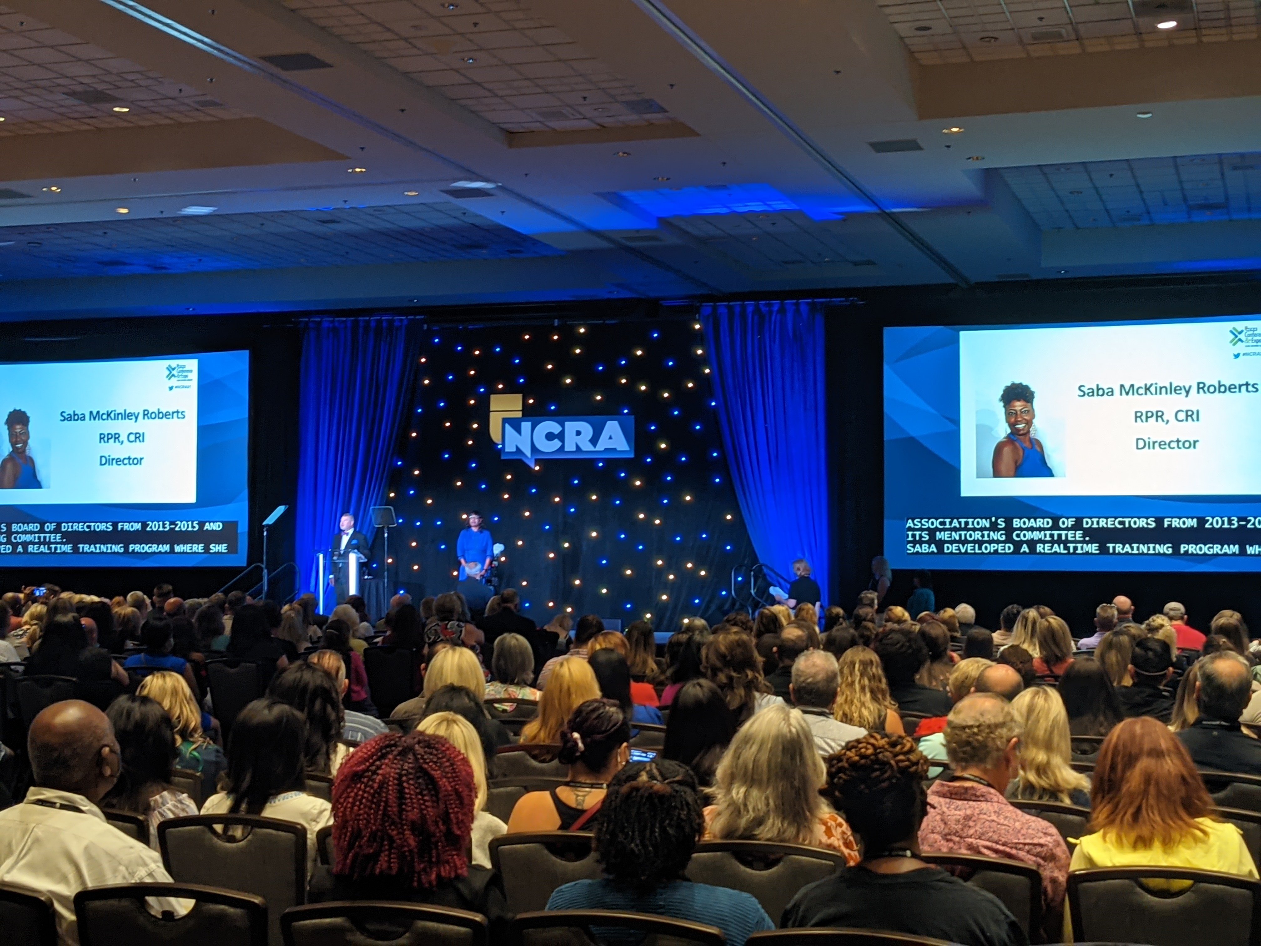 A picture of a packed auditorium. The audience is watching Saba McKinley Roberts leave the stage after being appointed to the NCRA board of directors.