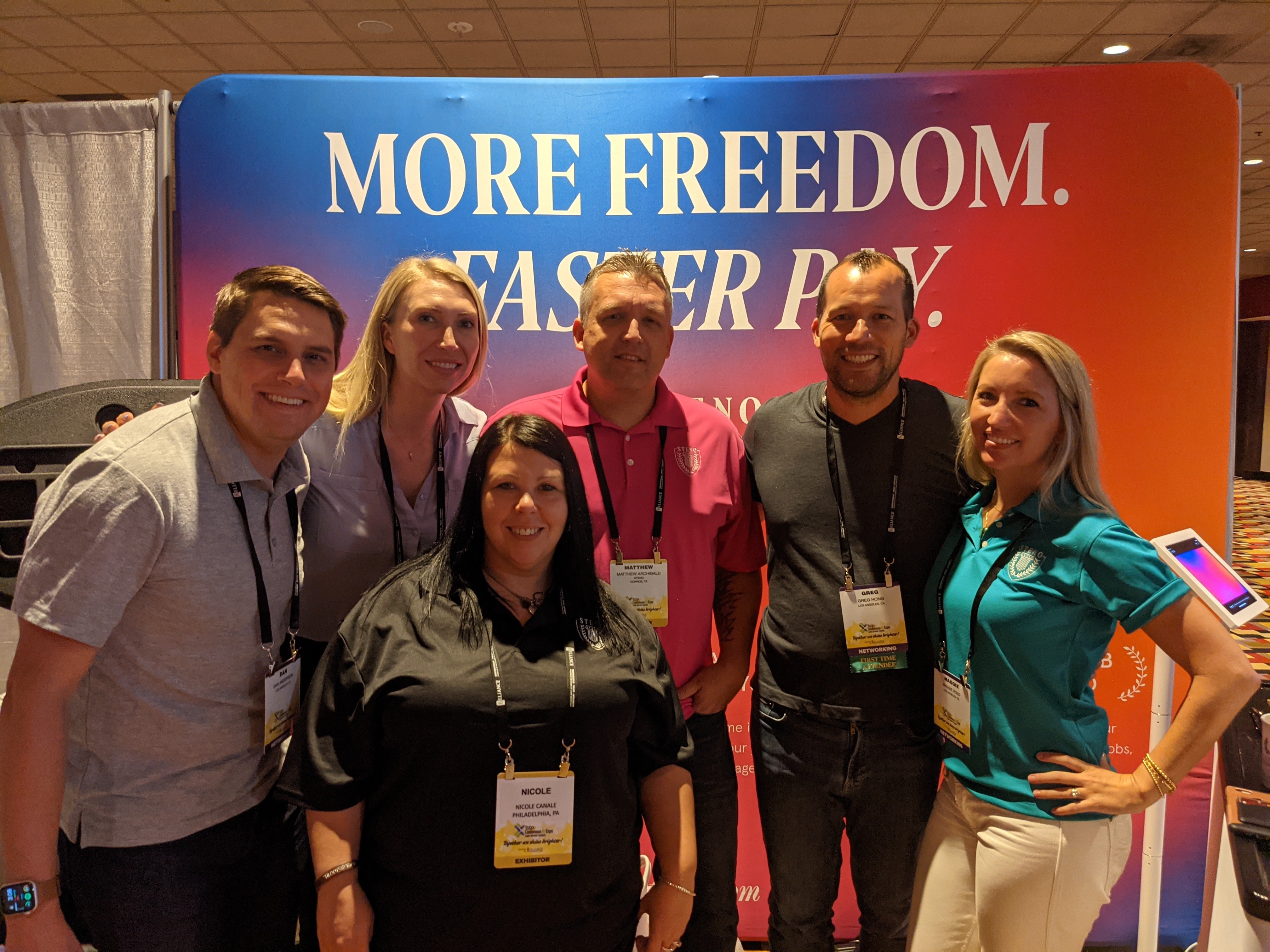 Six people smiling while standing in a booth at the NCRA expo hall. 