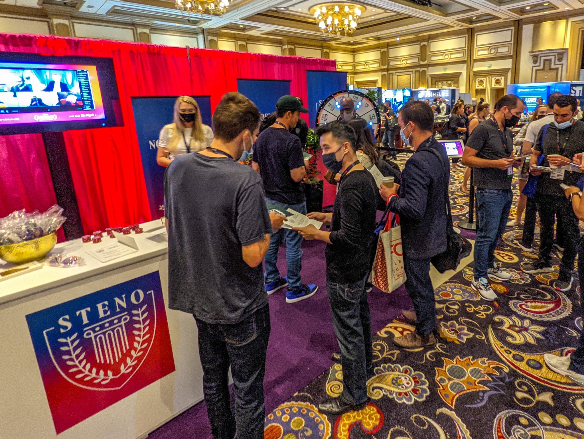 People talking in front of a booth with Steno branding and a light-up prize wheel