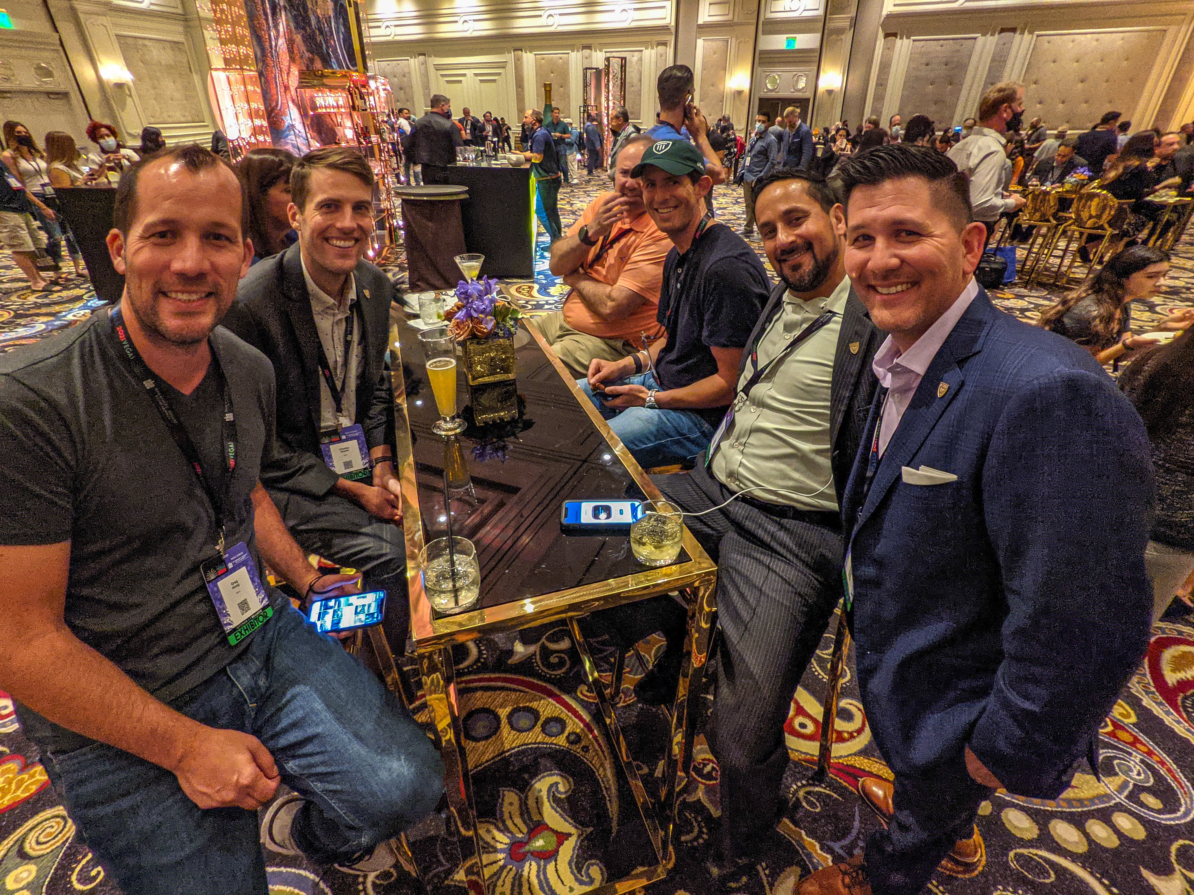 A group of men sitting around a table, looking at the camera, and smiling.