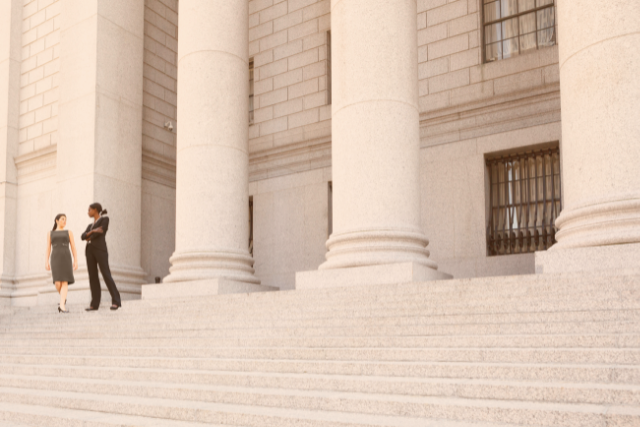 Two businesswomen standing on the steps to a courthouse.