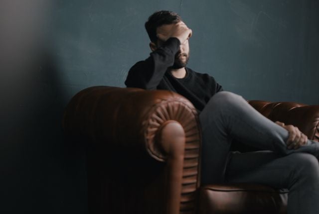 A man on a couch with his head in his hand.